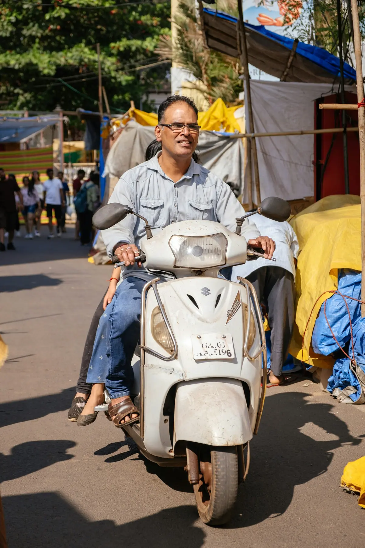 A man riding a white scooter through a market street.